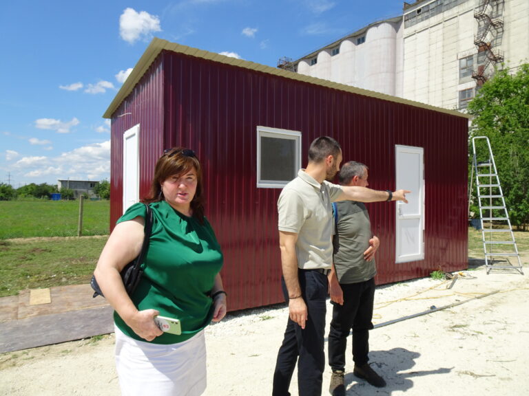 Zu sehen ist ein roter Container, der Vizebürgermeister zeigt Tierarzt Attila den Aufbau. Eine weitere Dame der Stadtverwaltung ist zu sehen.